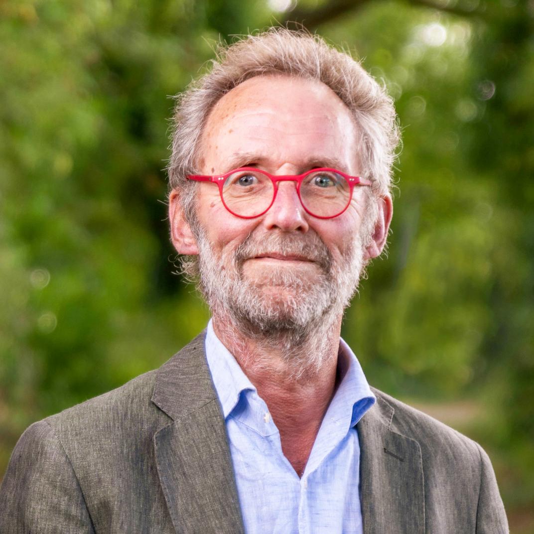 Foto wethouder Henk van der Goot: blond grizjig kort haar, lichte baard en snor, bril rood montuur, bruin jasje en lichtblauwe blouse